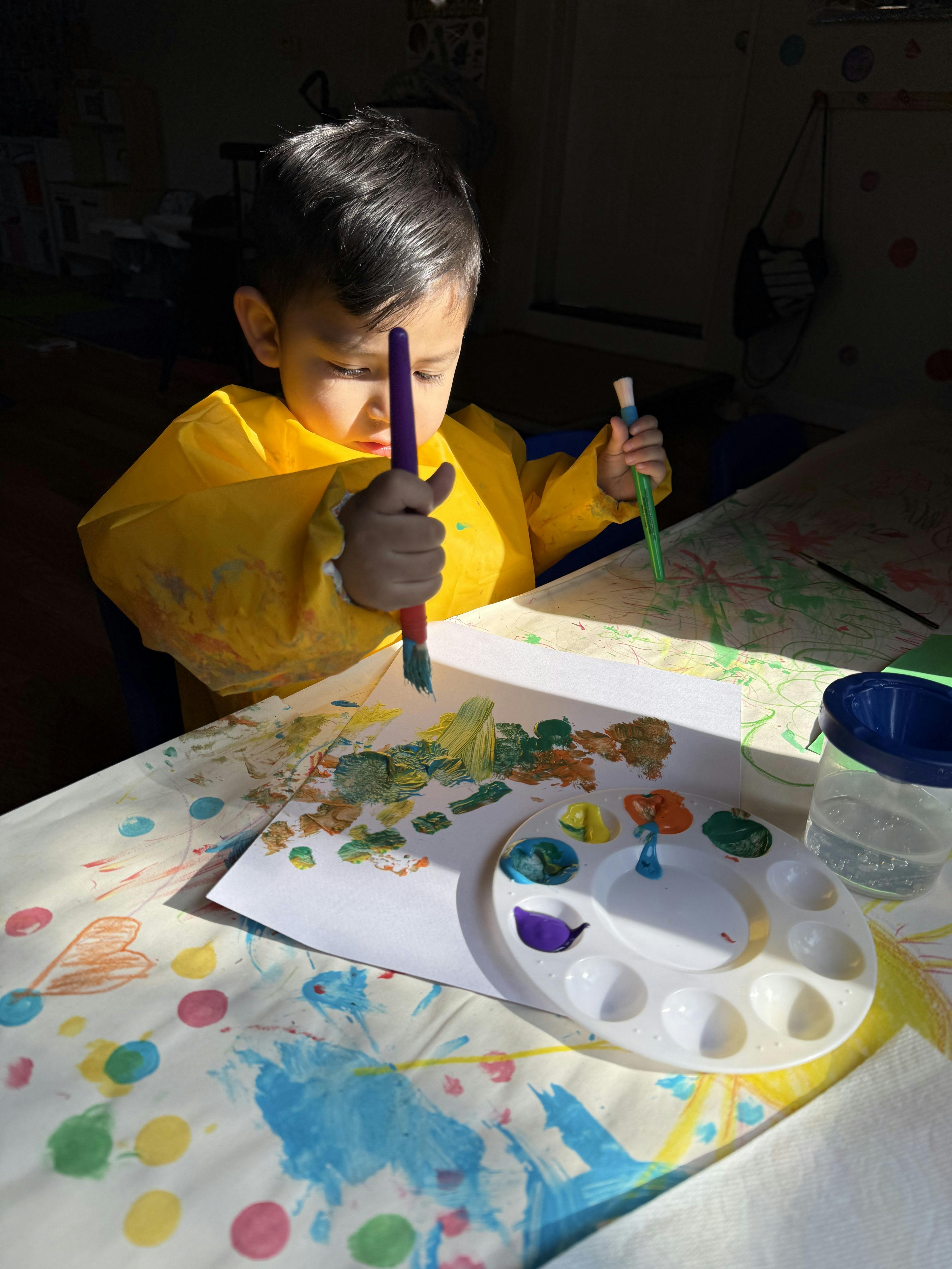 Child in a yellow smock painting with a brush and palette