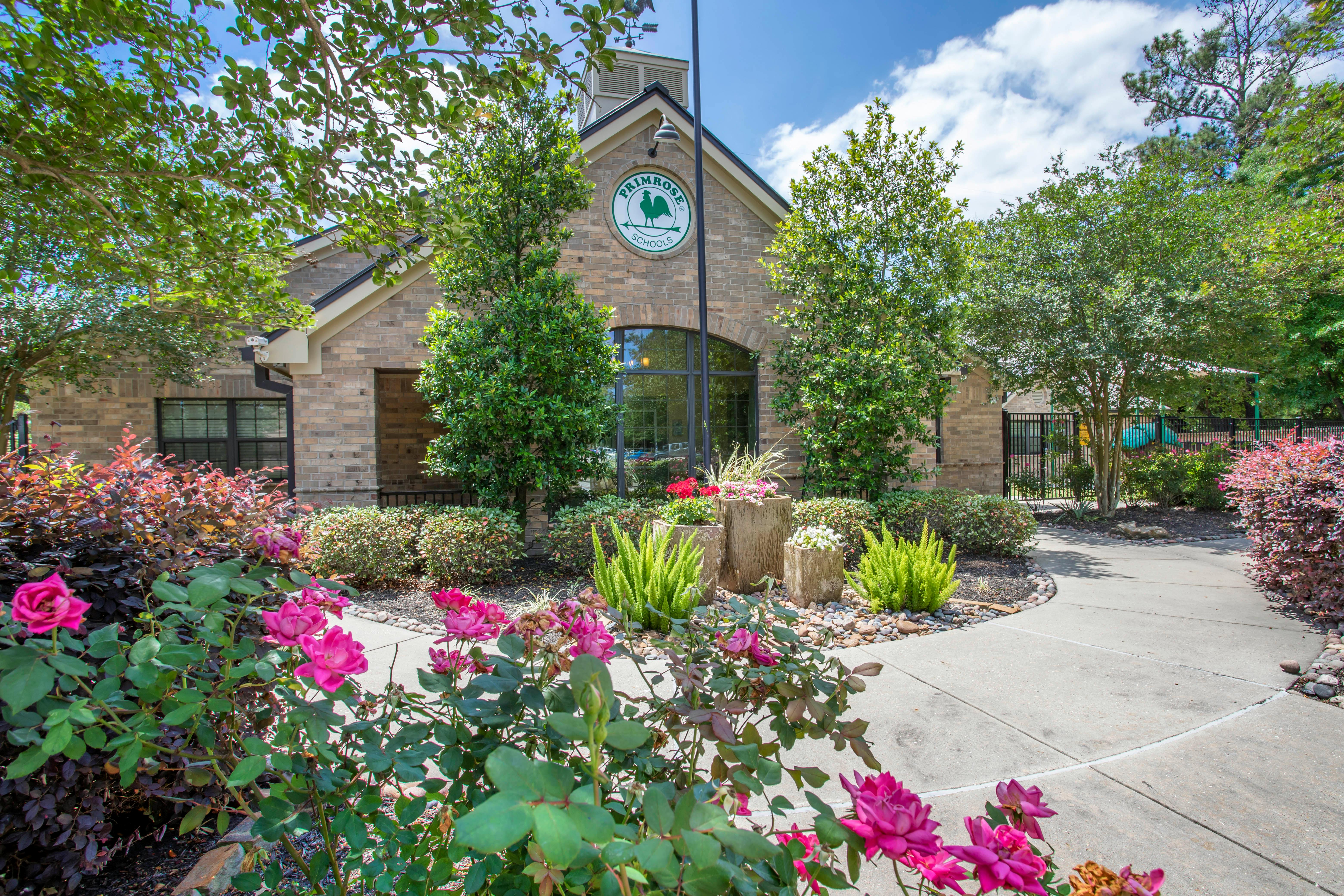 Brick building with "Primrose Schools" sign, surrounded by flowering bushes and trees