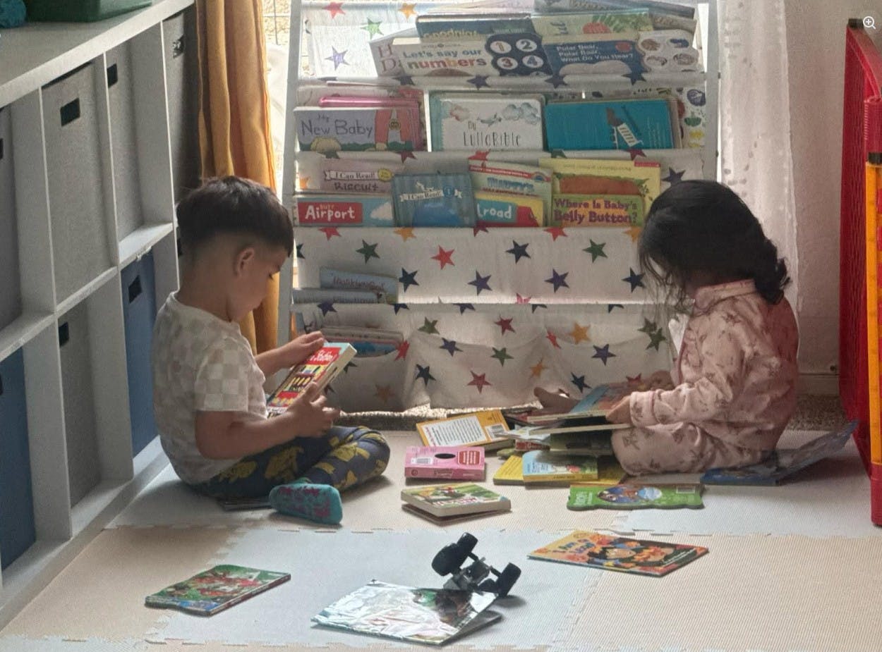 Two children sitting on the floor reading books near a bookshelf