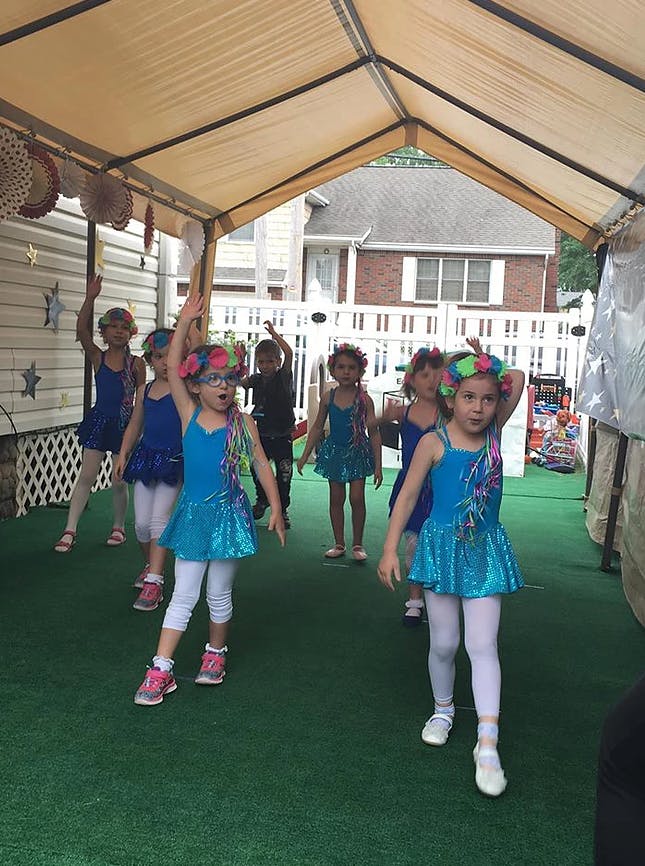 Children in blue dresses and headbands dancing under a canopy