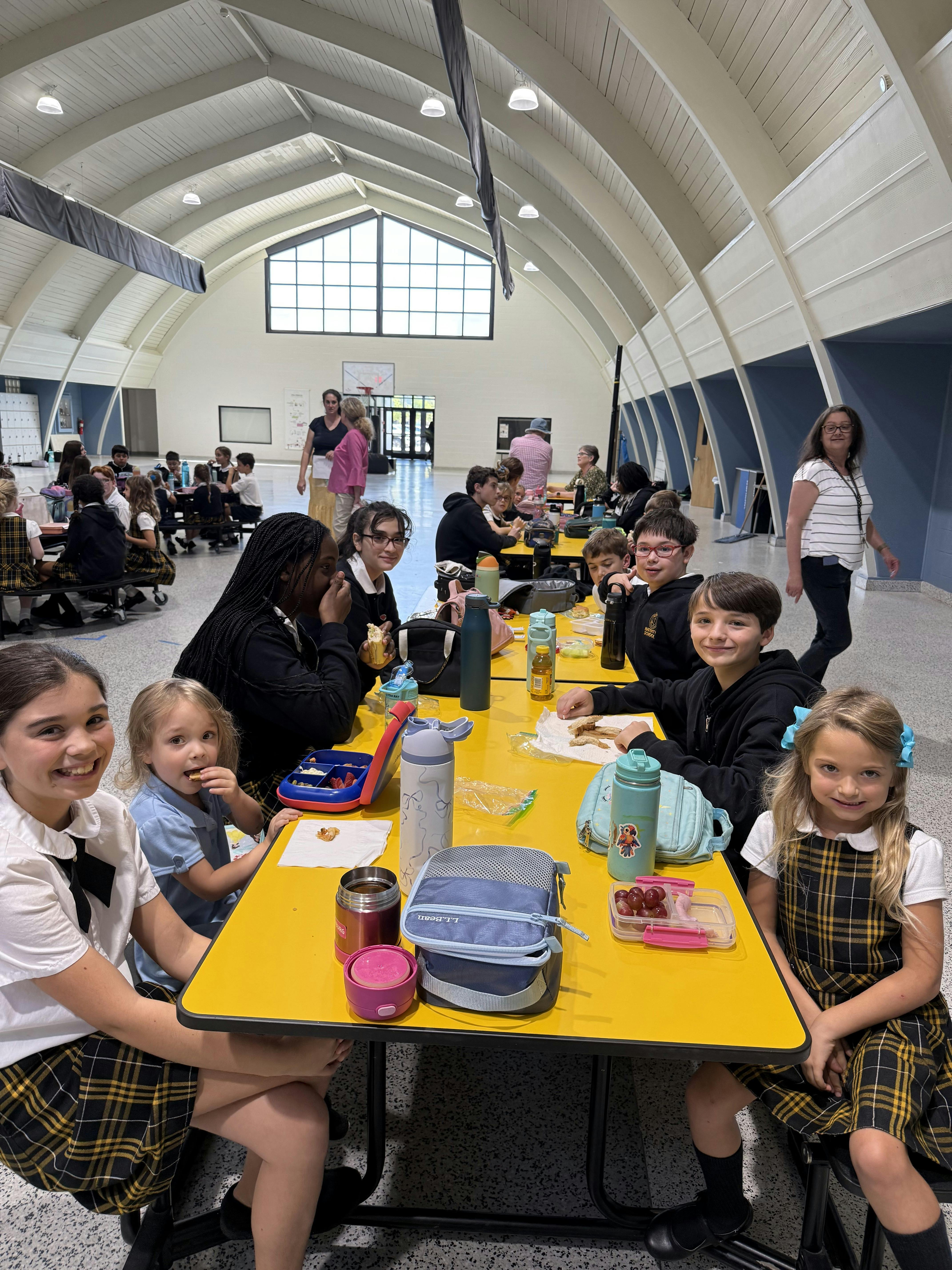 Children eating lunch together at yellow tables in a large room