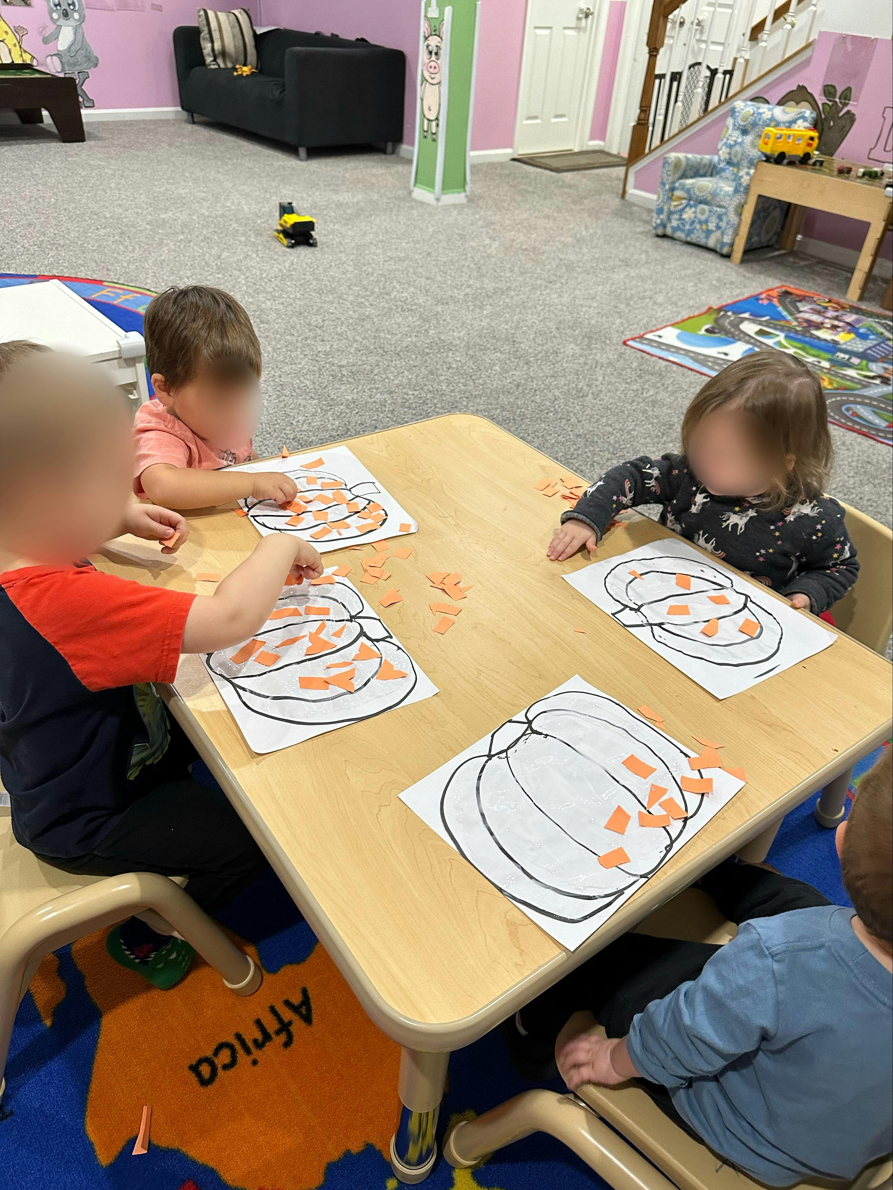Children at a table doing a craft with pumpkin outlines and orange paper pieces
