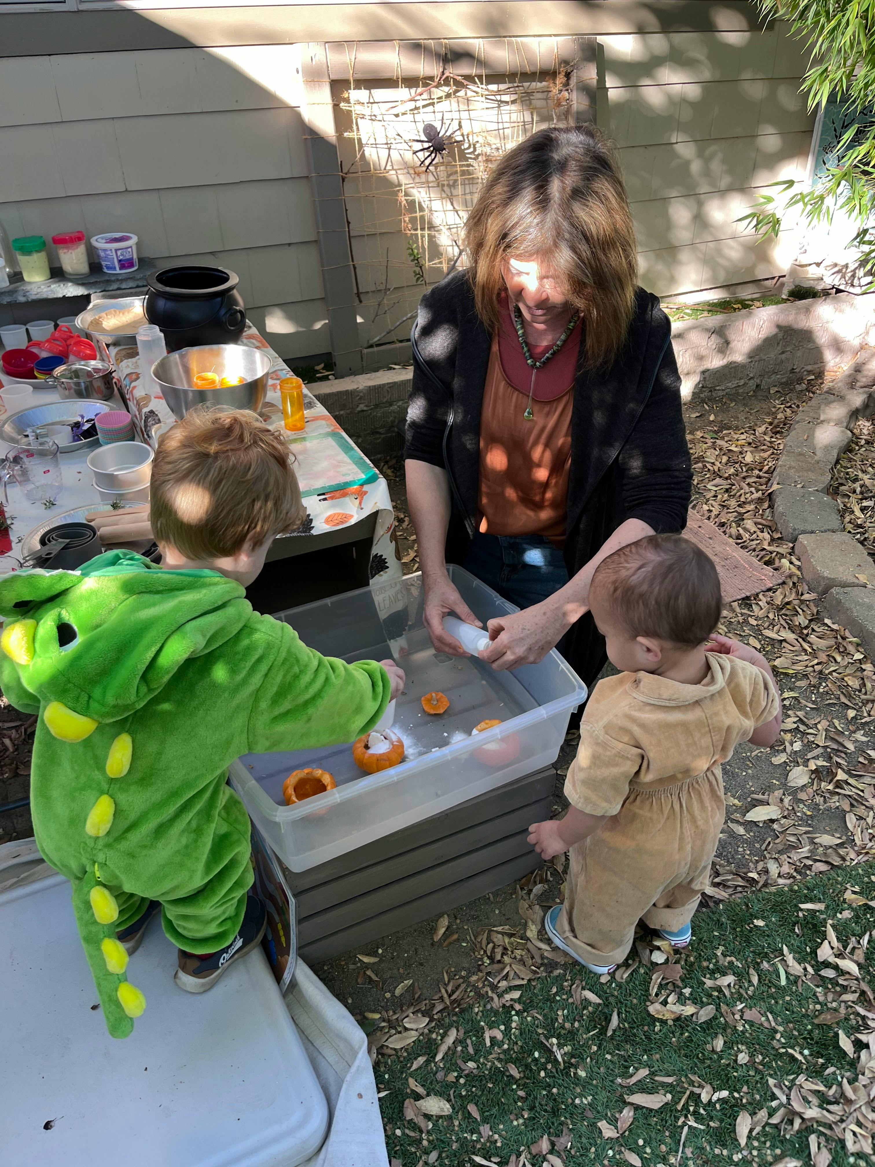 Adult and two children playing with water and toys in a bin outdoors