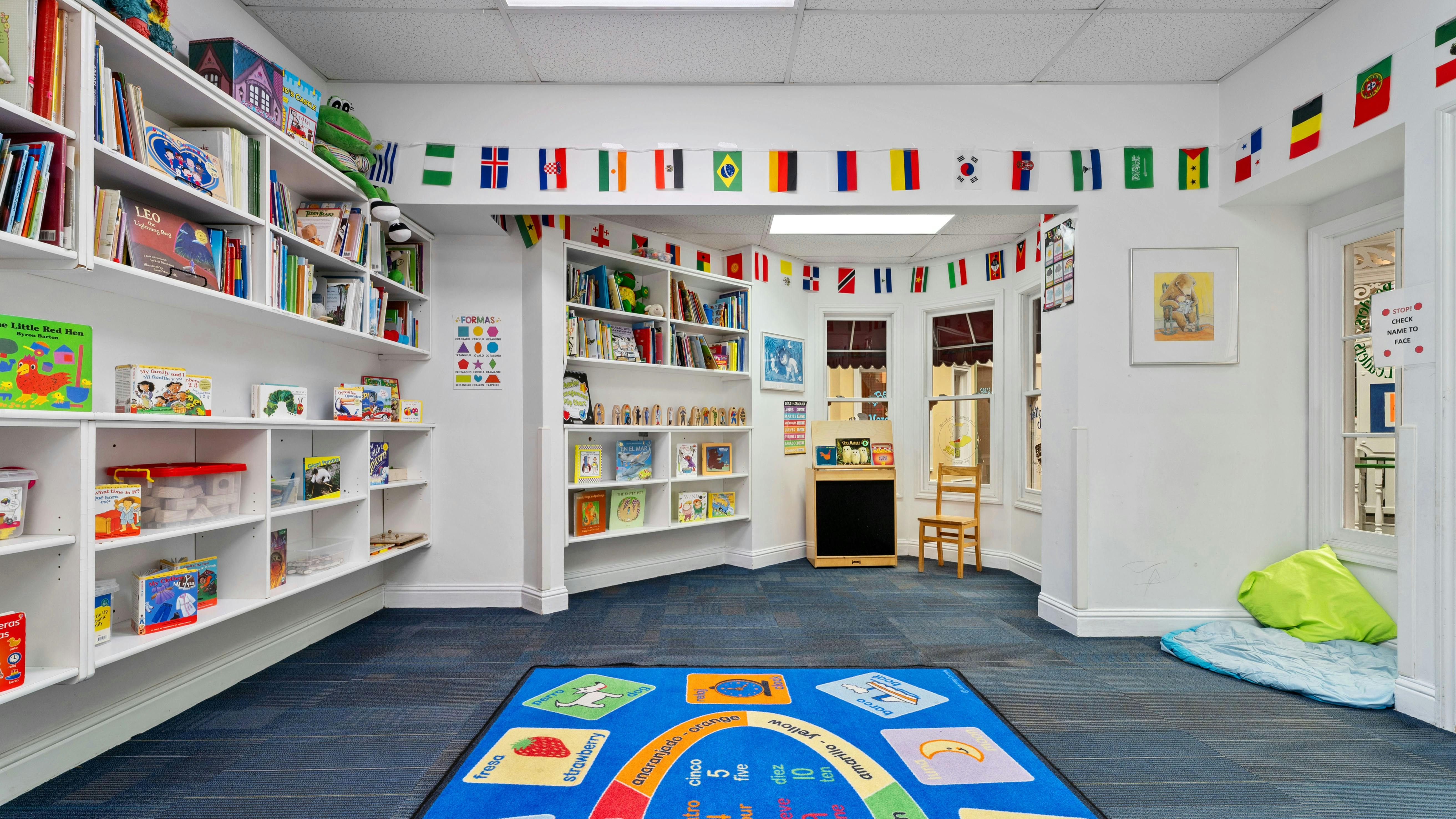 Classroom with bookshelves, a blue rug, and windows decorated with international flags
