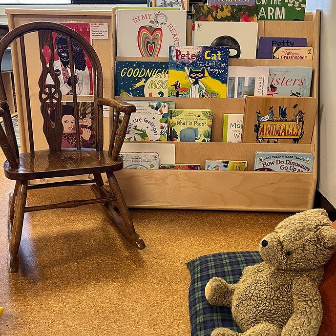 Child-sized rocking chair next to a bookshelf with children's books and a teddy bear