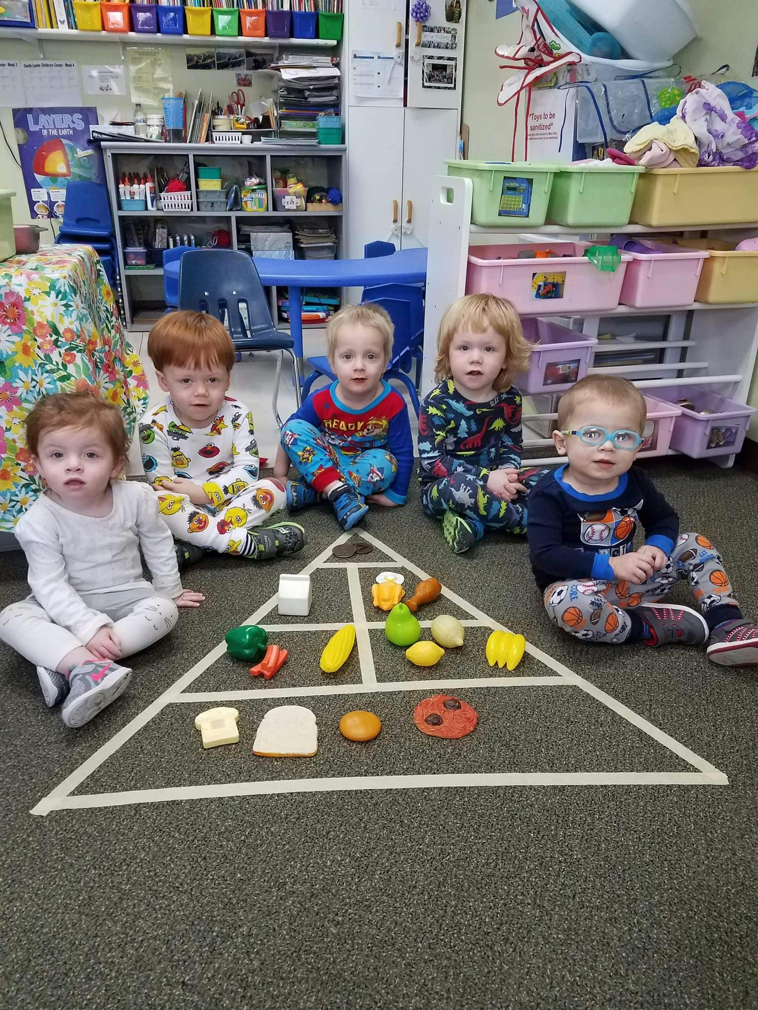 Five children sitting around a food pyramid made of tape on the floor