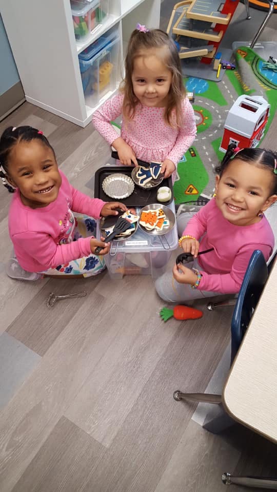 Three children playing with toy food and dishes on the floor