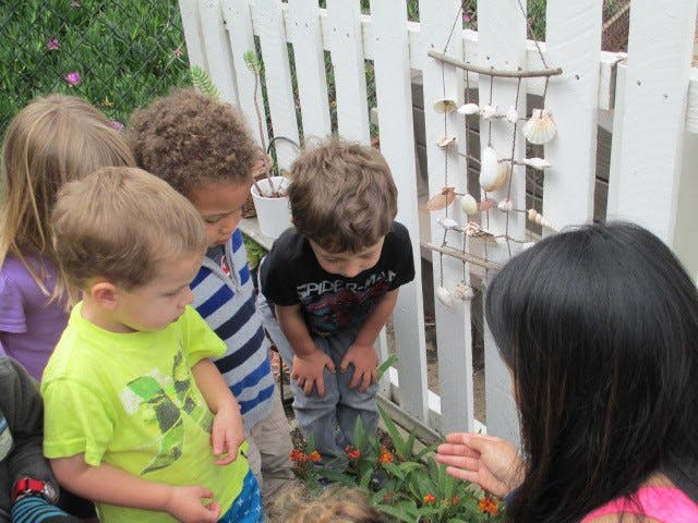 Four children and one adult looking at a seashell decoration on a fence