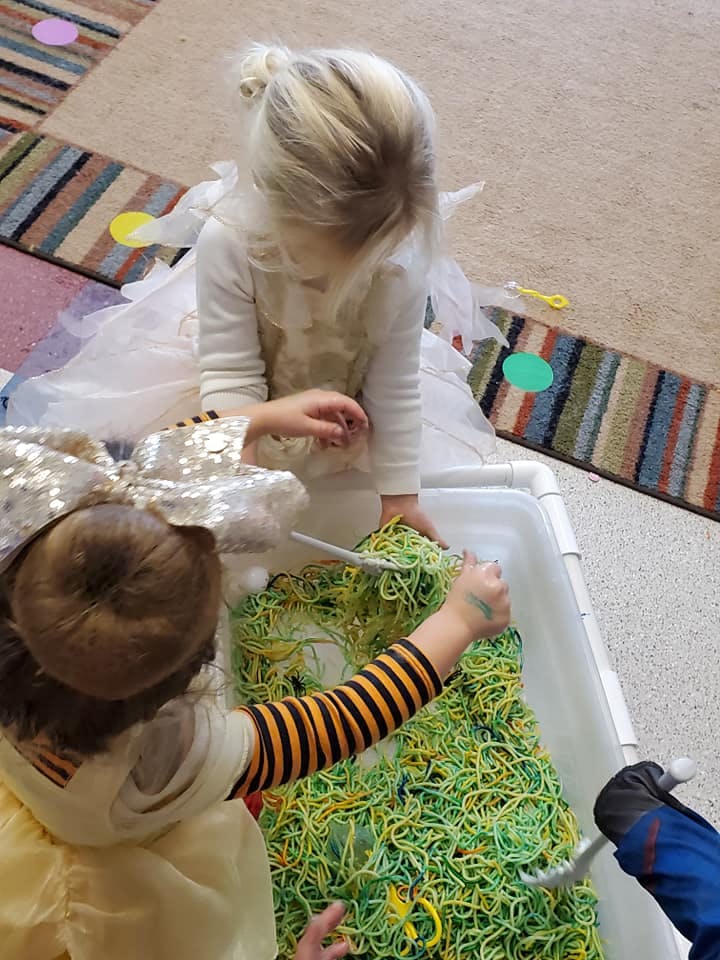 Two children playing with green and yellow string in a white bin
