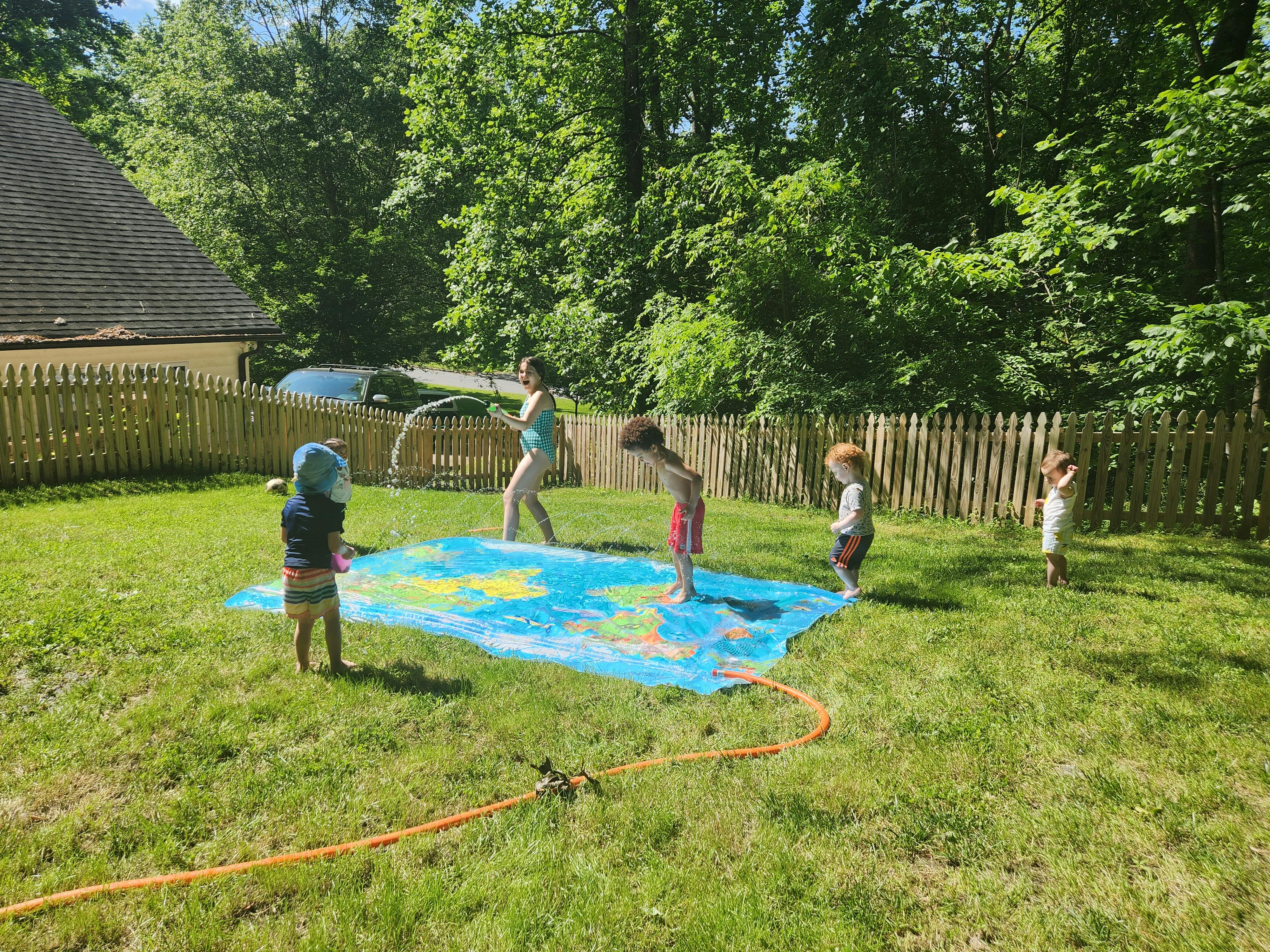 Person and children playing with a water mat in a grassy yard