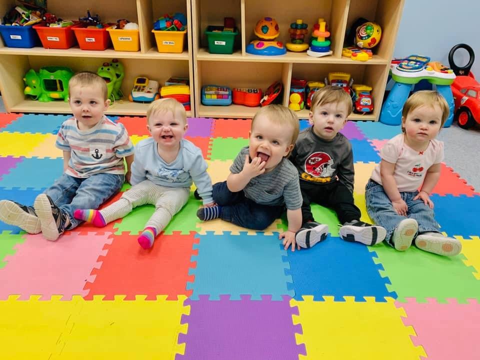 Five children sitting on a colorful mat in a playroom