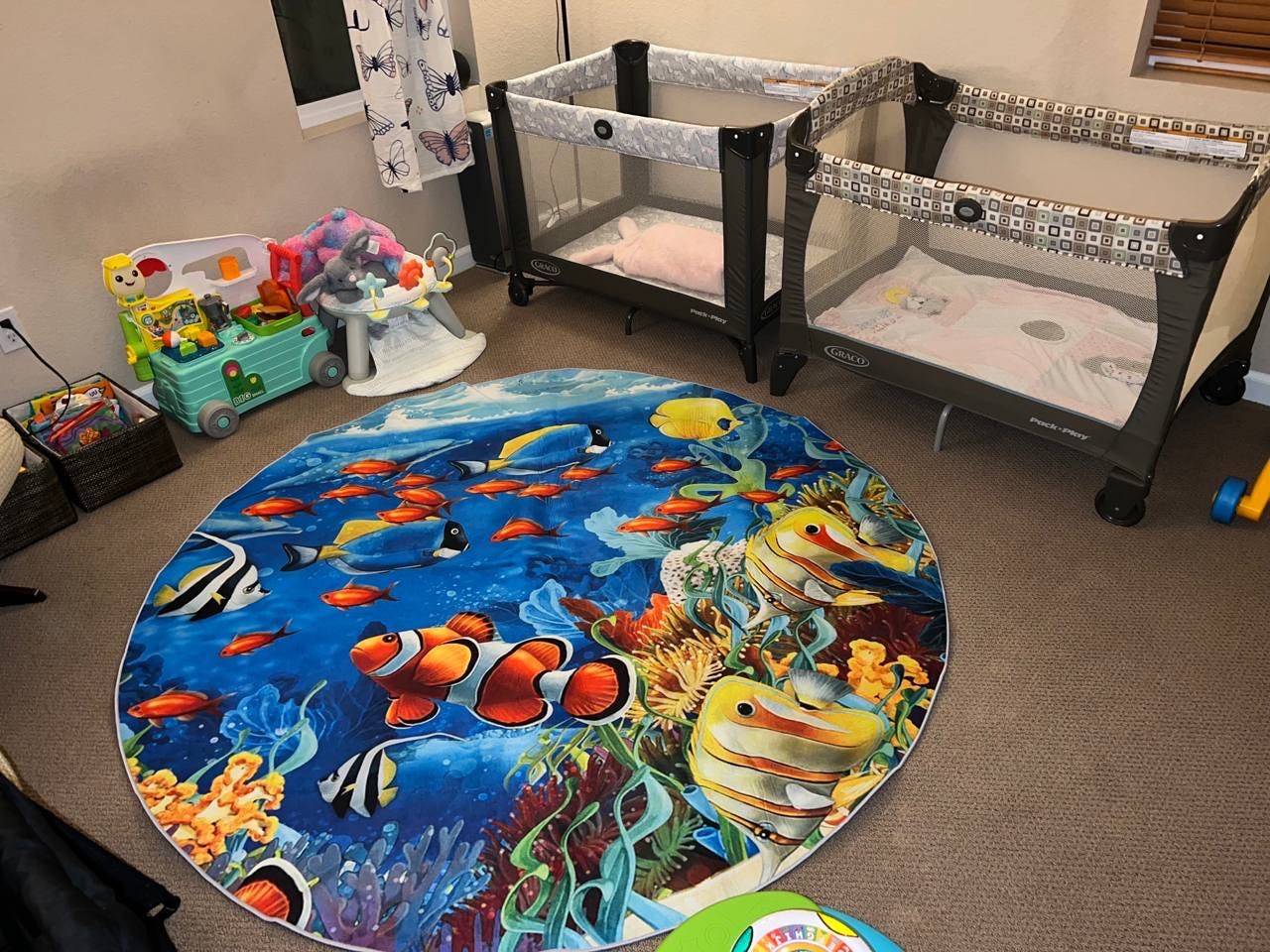 Two portable cribs and a round rug with an underwater fish design