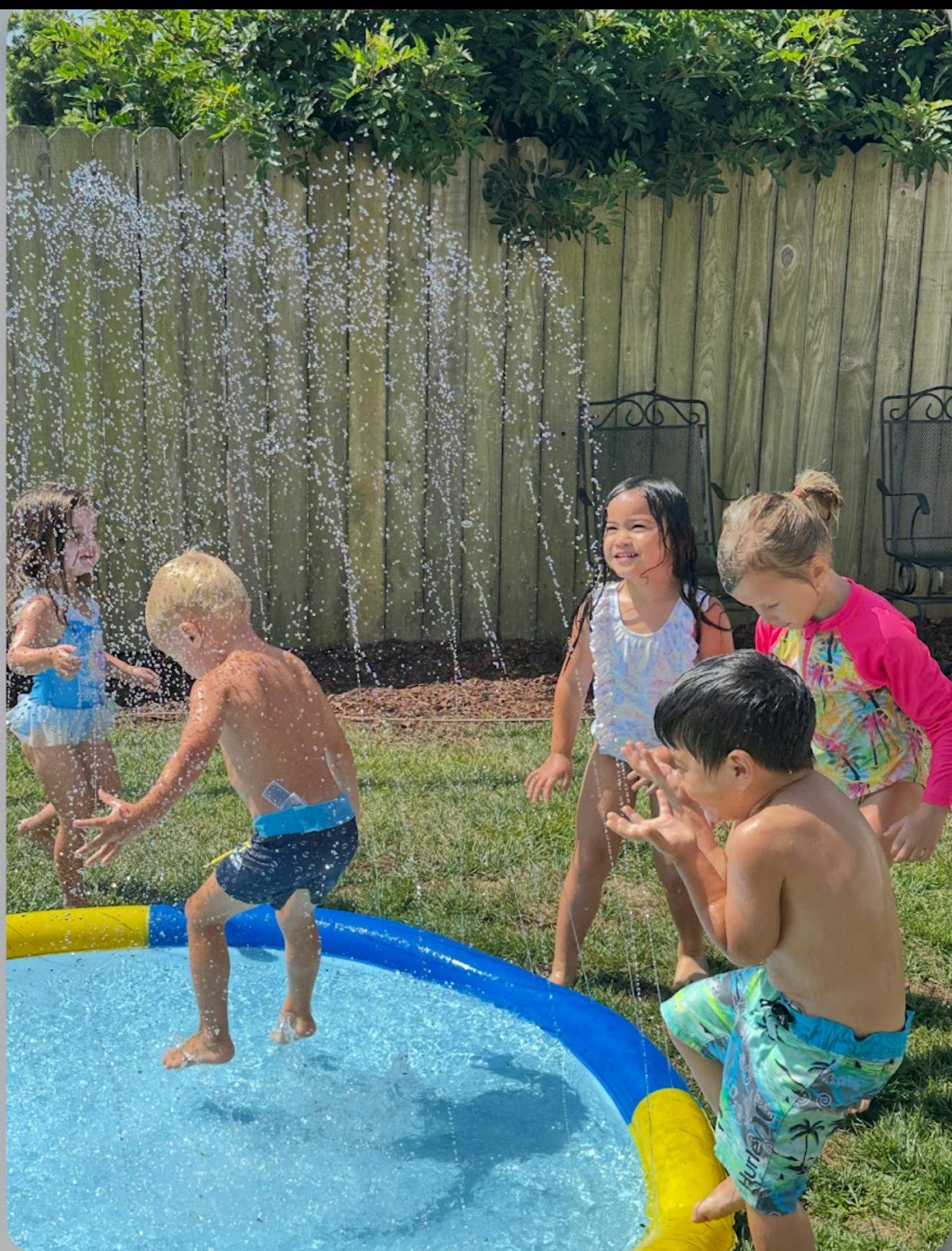 Children playing in a small backyard water pool with a sprinkler