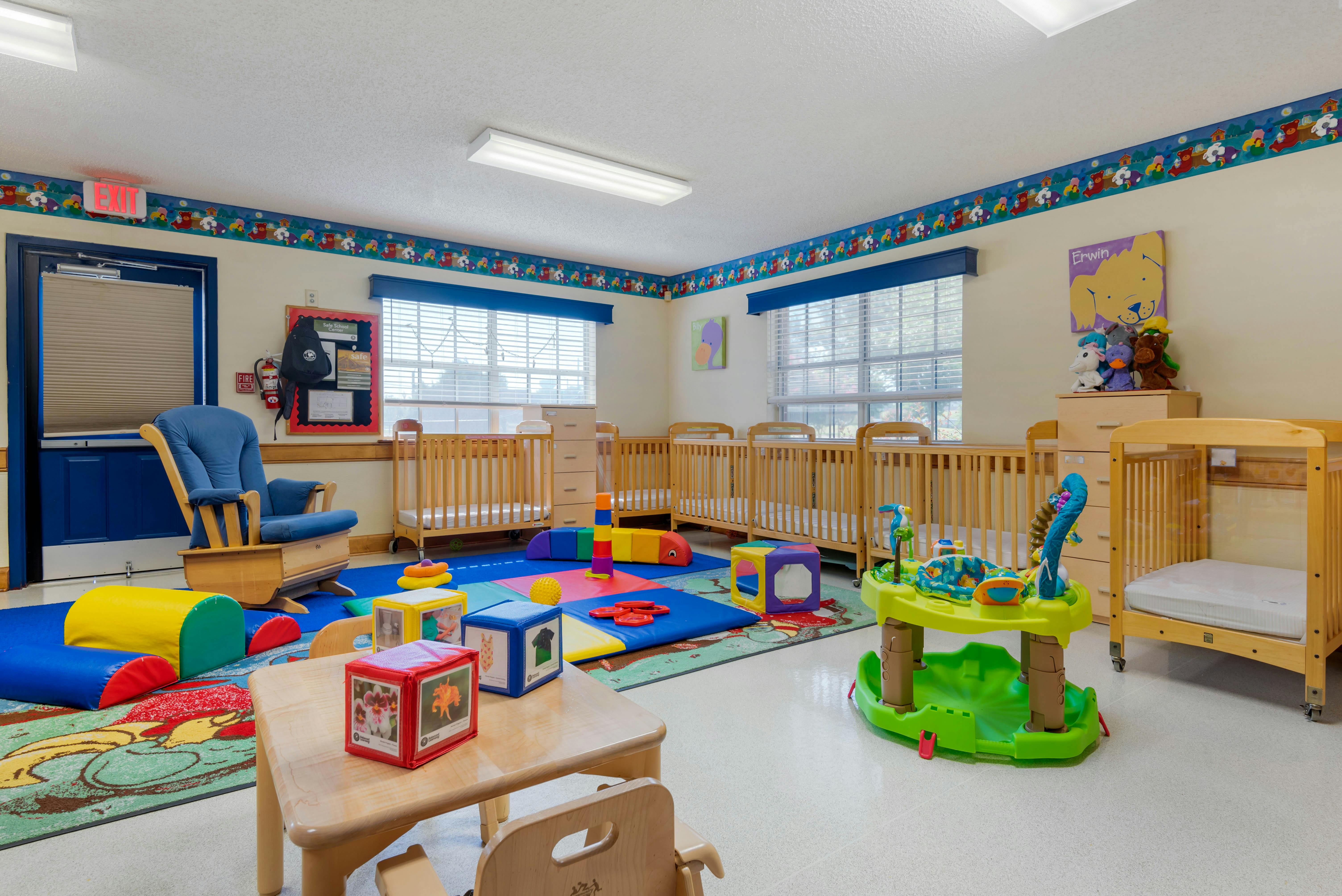 Classroom with multiple cribs, a rocking chair, and play mats on the floor