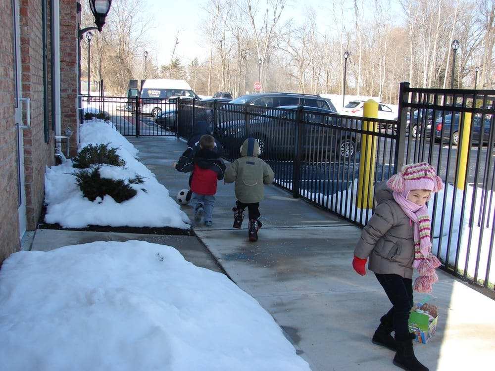 Three children walking on a snowy sidewalk next to a fence