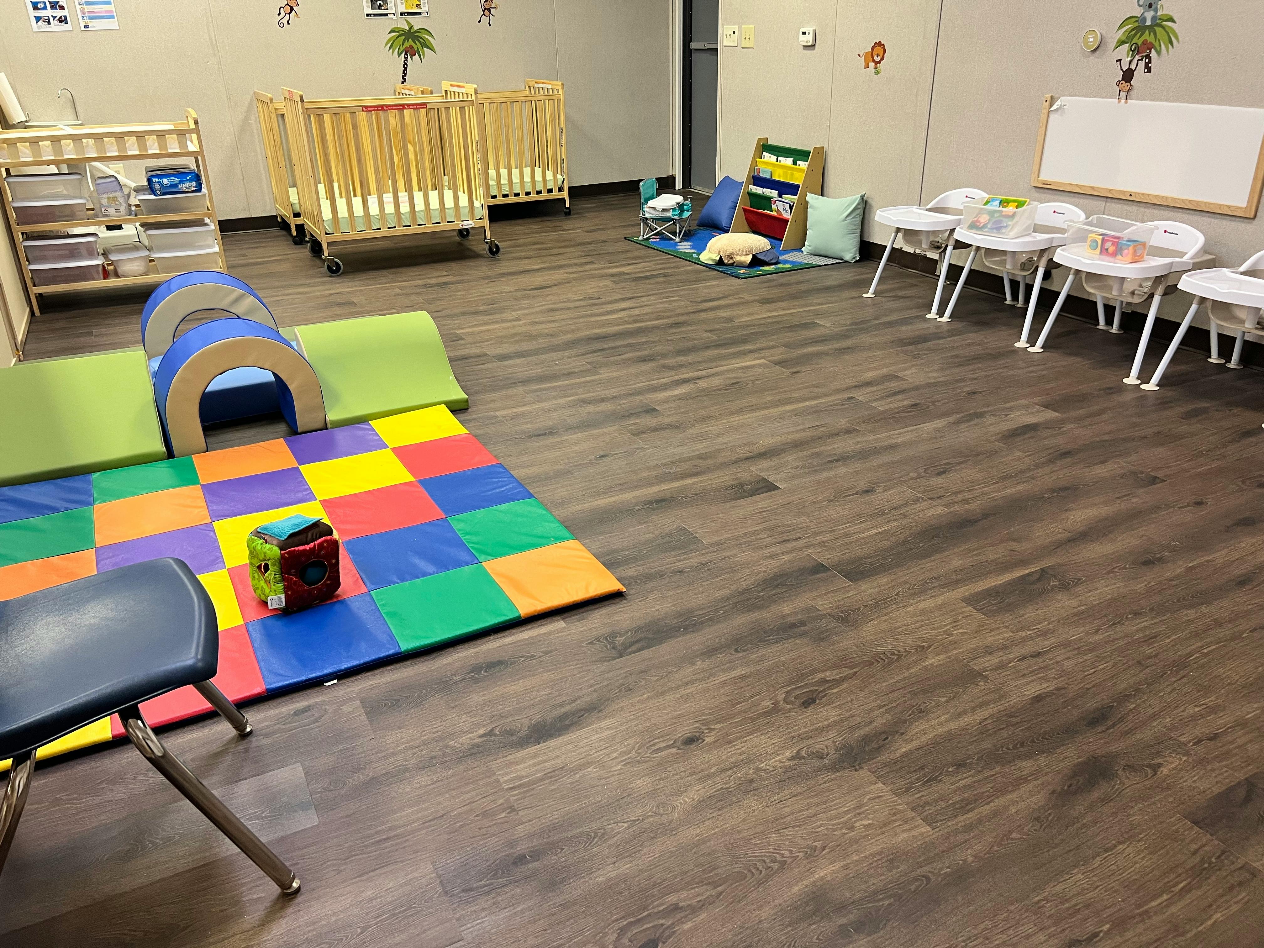Playroom with cribs, high chairs, and colorful play mats