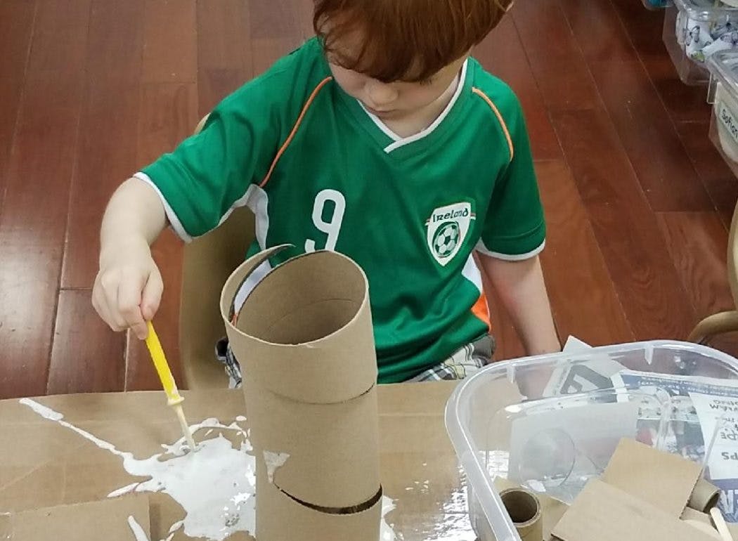 Child gluing cardboard tubes together with a yellow applicator