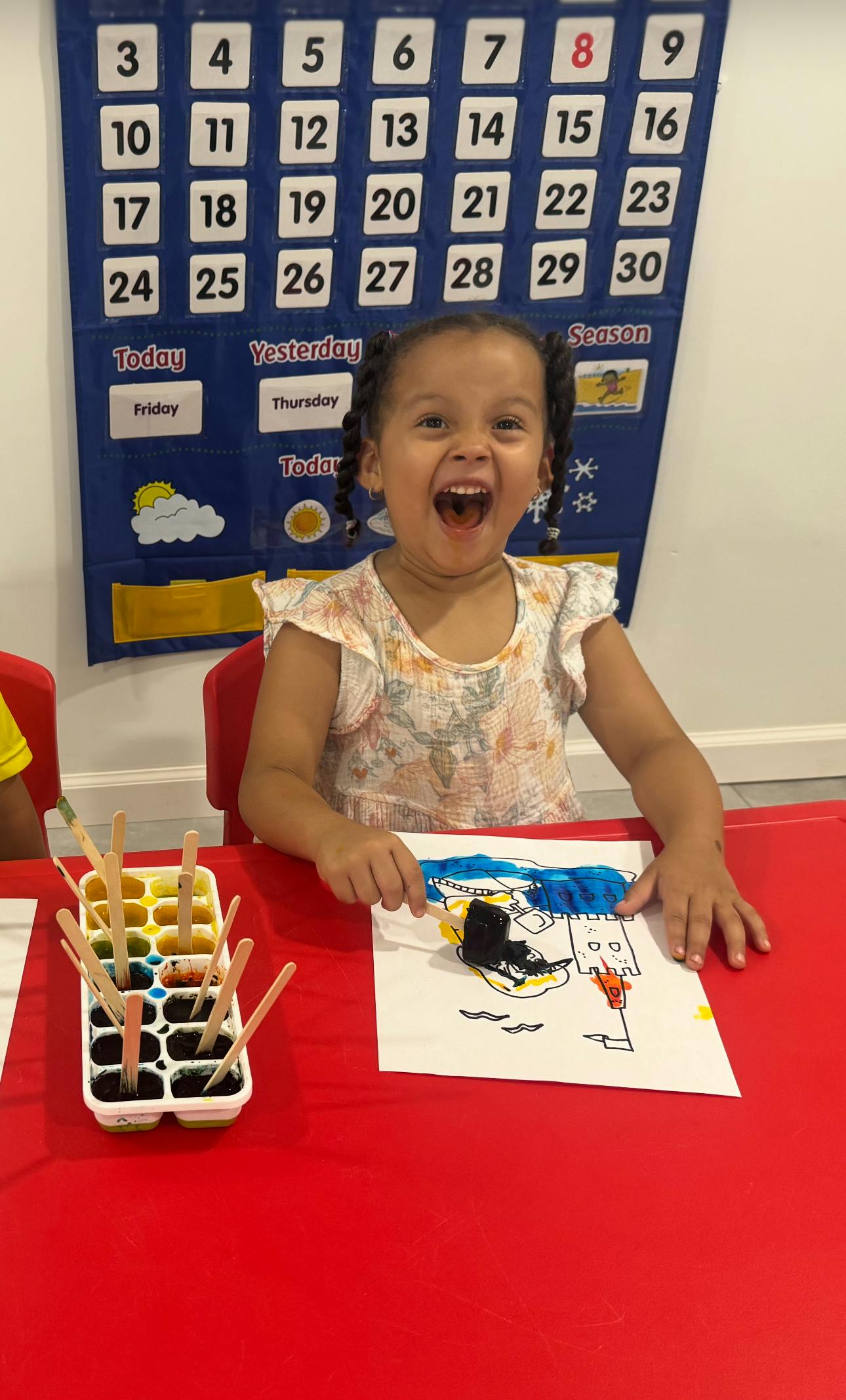 Child sitting at a table with a drawing and a paint palette