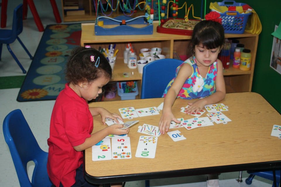 Two children playing with cards at a table in a classroom