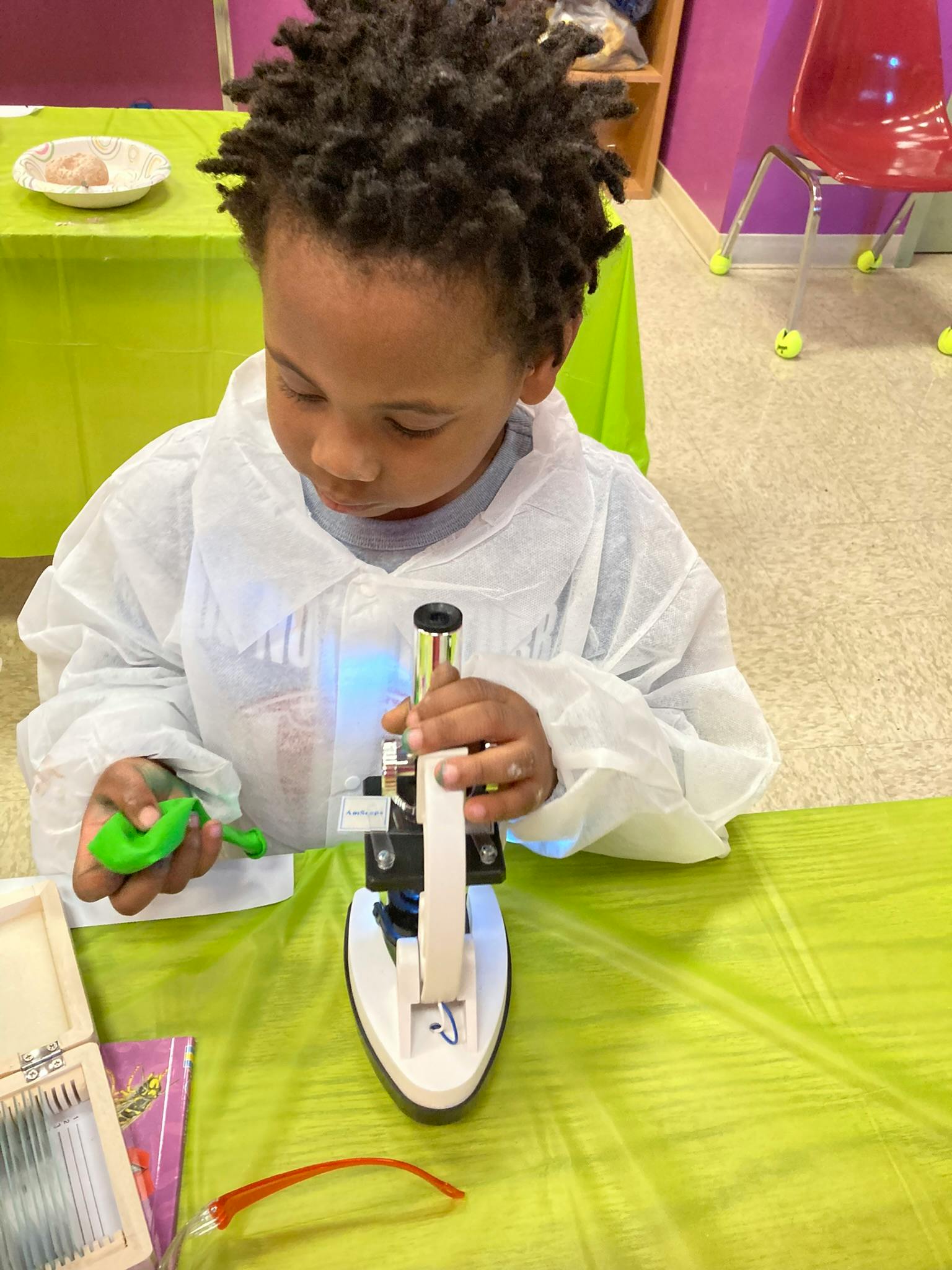 Child in a lab coat looking into a microscope