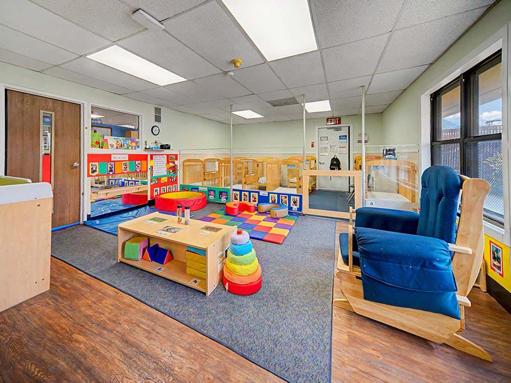 Classroom with cribs, play mats, and a rocking chair