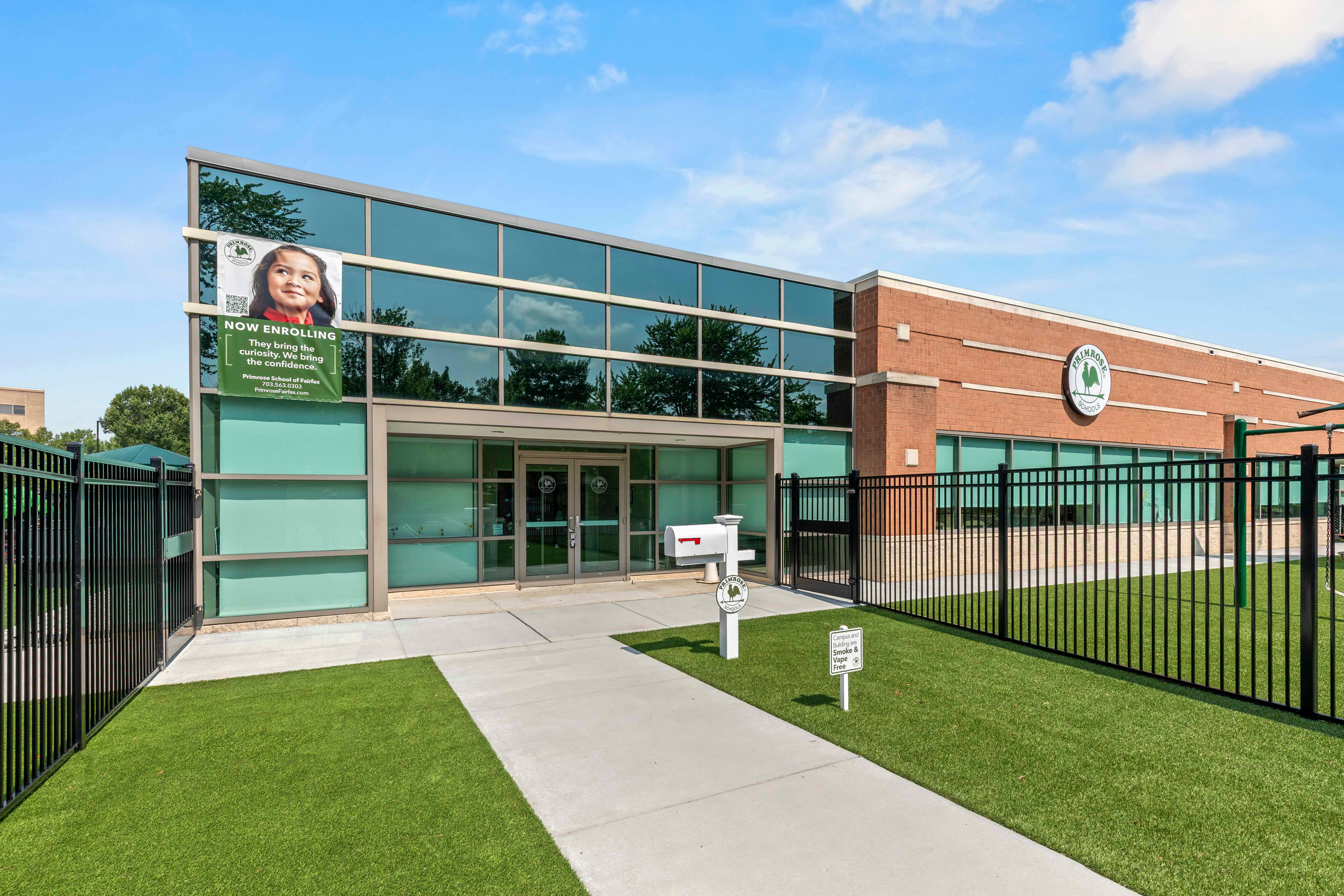 Modern school building with glass facade and brick, a green banner reads "NOW ENROLLING"