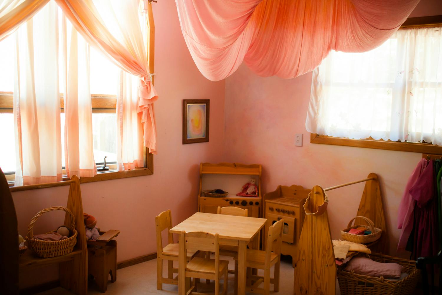 Children's play area with small wooden table and chairs, pink walls, and sheer drapes