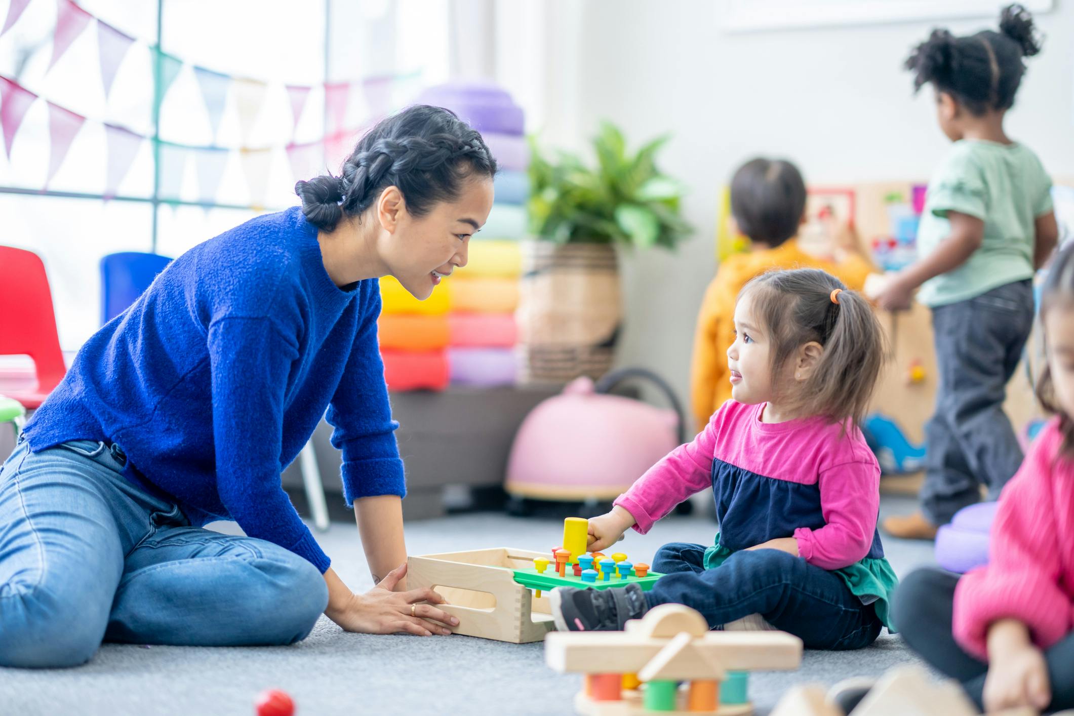 Adult and child playing with a peg toy on the floor in a brightly lit room