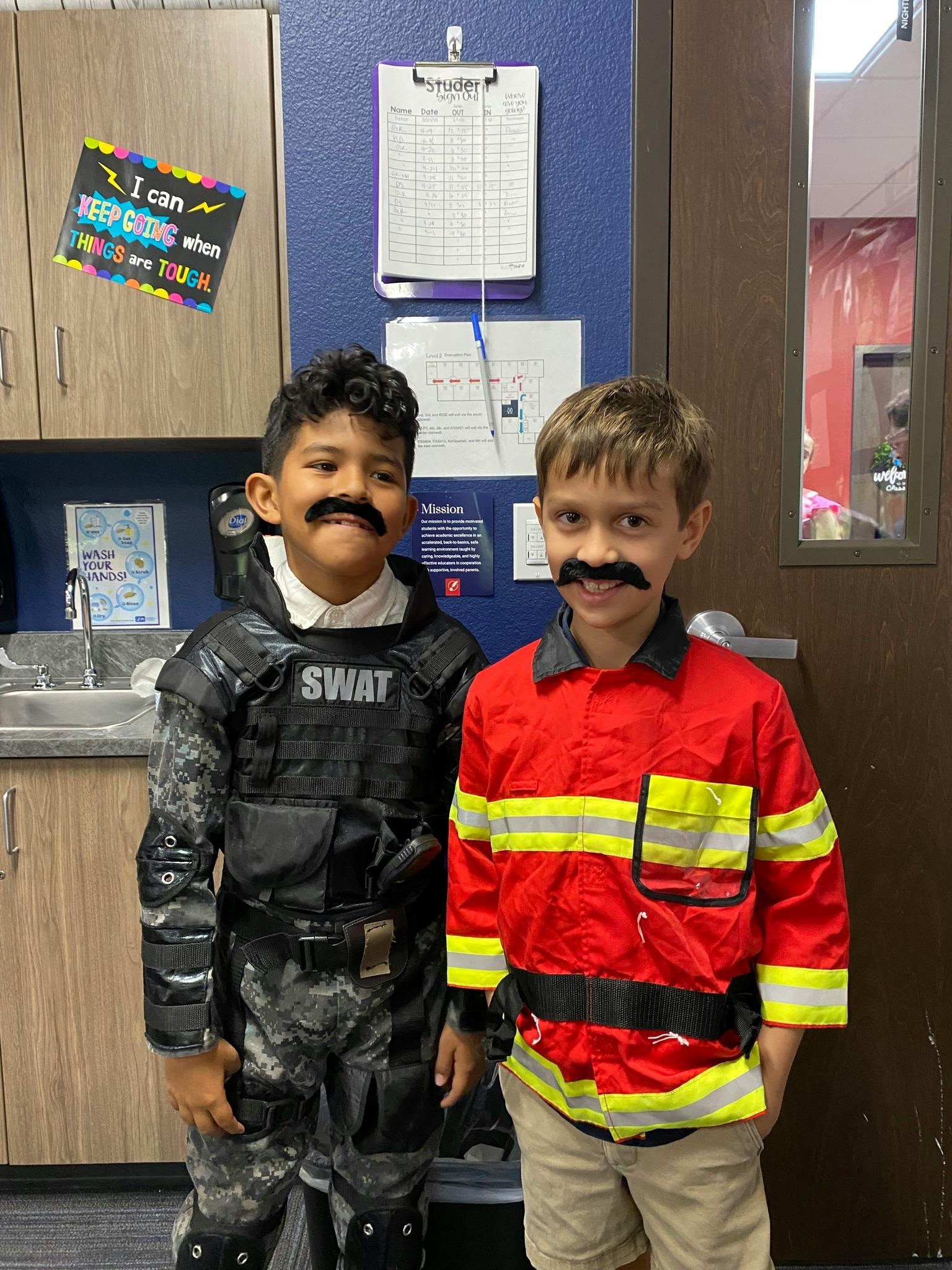 Two children in costumes with fake mustaches, one in SWAT gear, one in a firefighter jacket