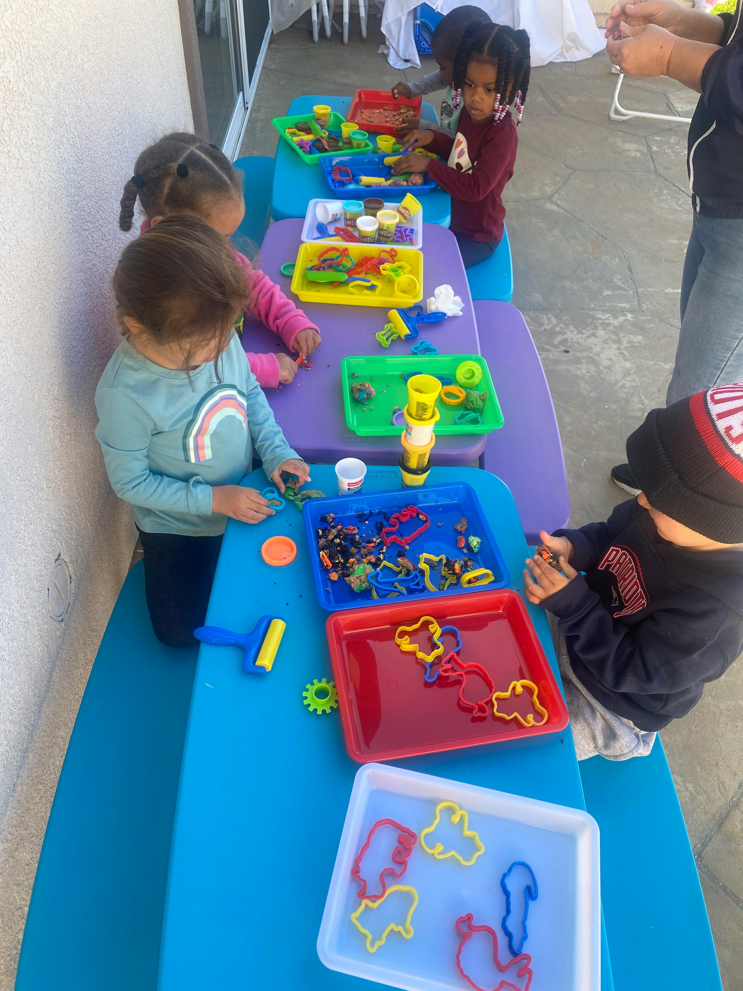 Children playing with colorful trays of toys and cookie cutters at a table
