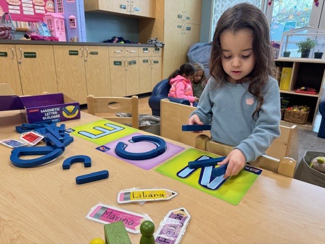 Child building letters with blue magnetic pieces in a classroom
