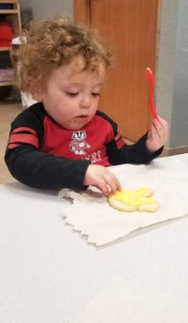 Child decorating a cookie with yellow frosting