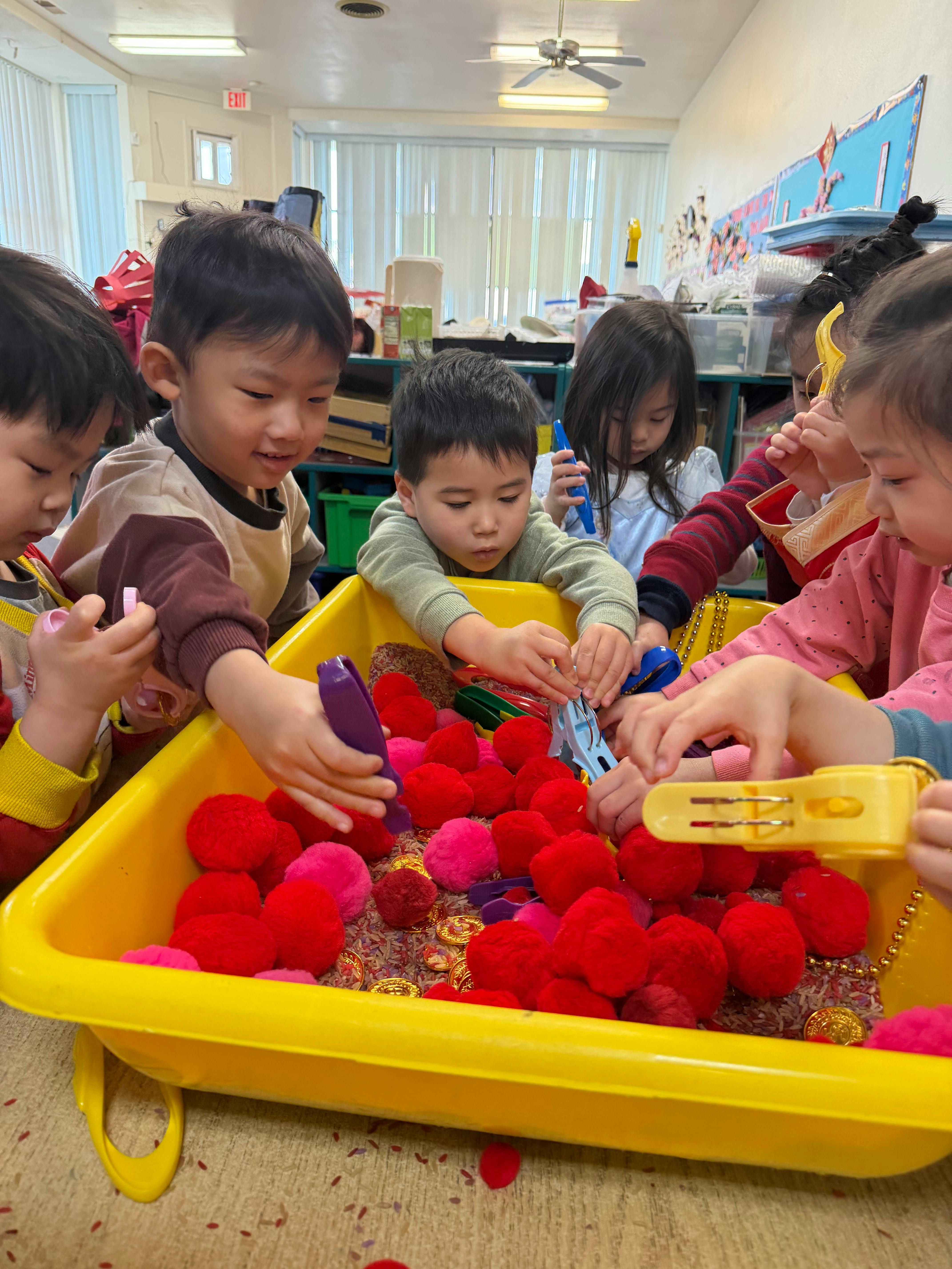 Group of children using tongs to pick up pom-poms in a sensory bin