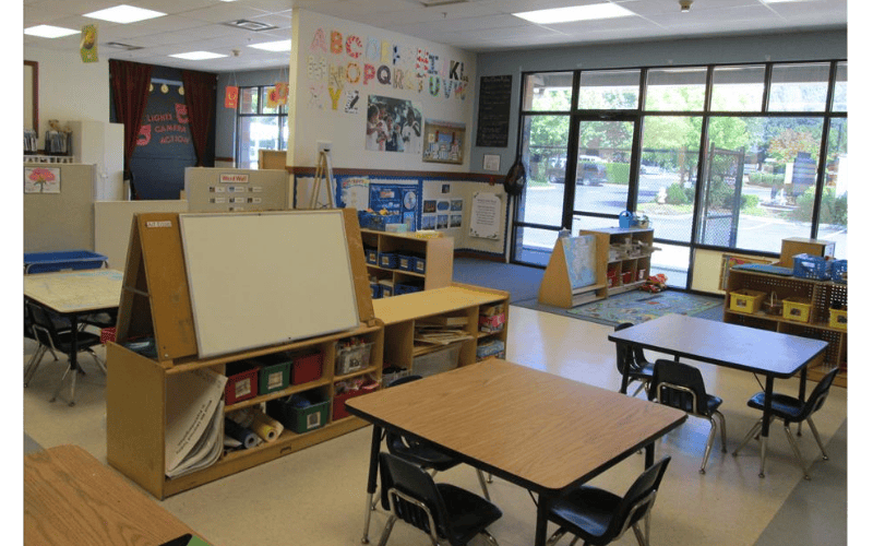 An empty early childhood classroom with small tables, chairs, and shelves