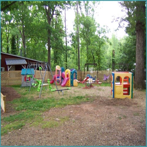 Playground equipment including swings and slides in a wooded area