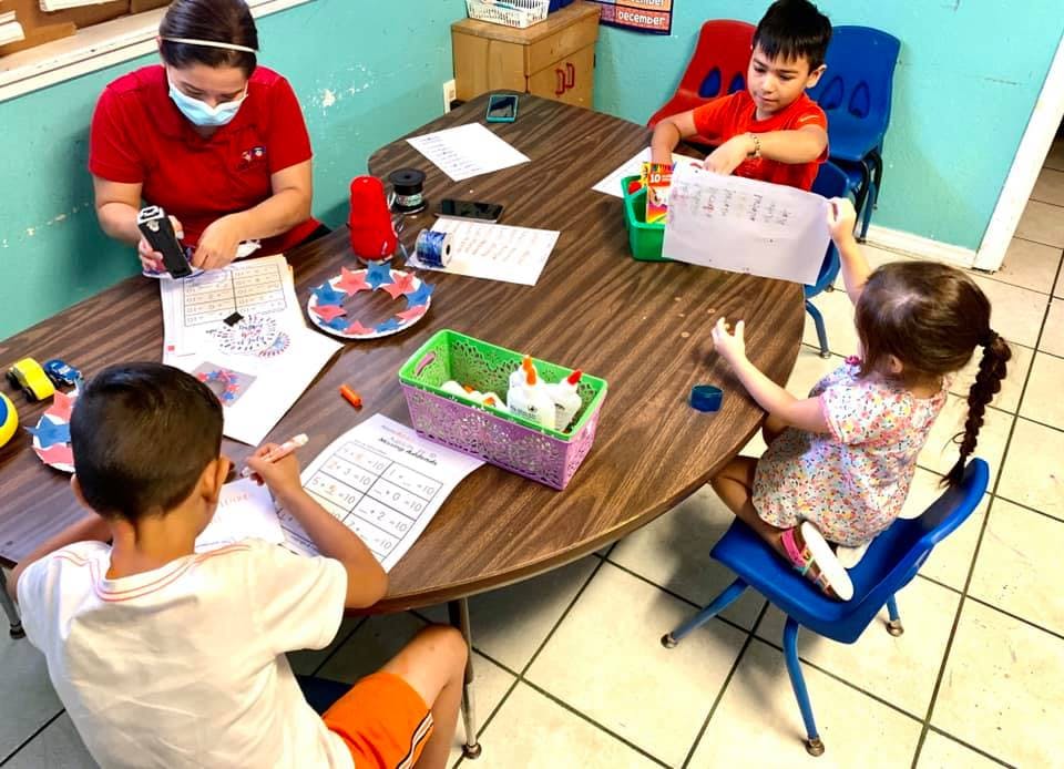 Adult and three children at a table with papers and art supplies