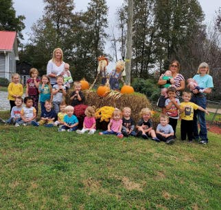 Adults and children sitting and standing on a grassy hill with pumpkins