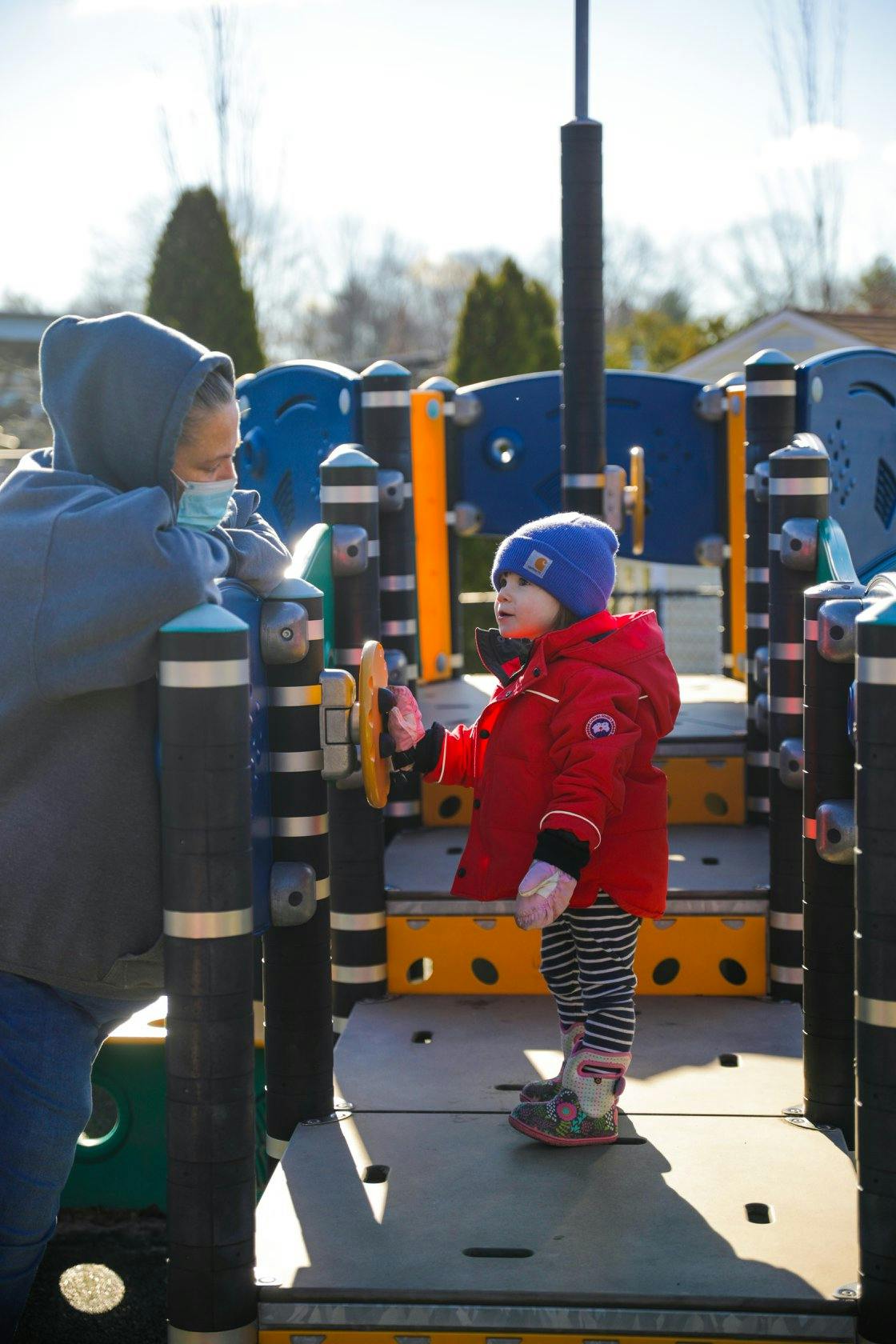 Person in mask and child on playground structure at a playground