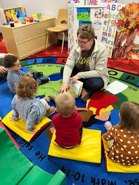 Adult reading a book to children sitting on a colorful rug in a classroom