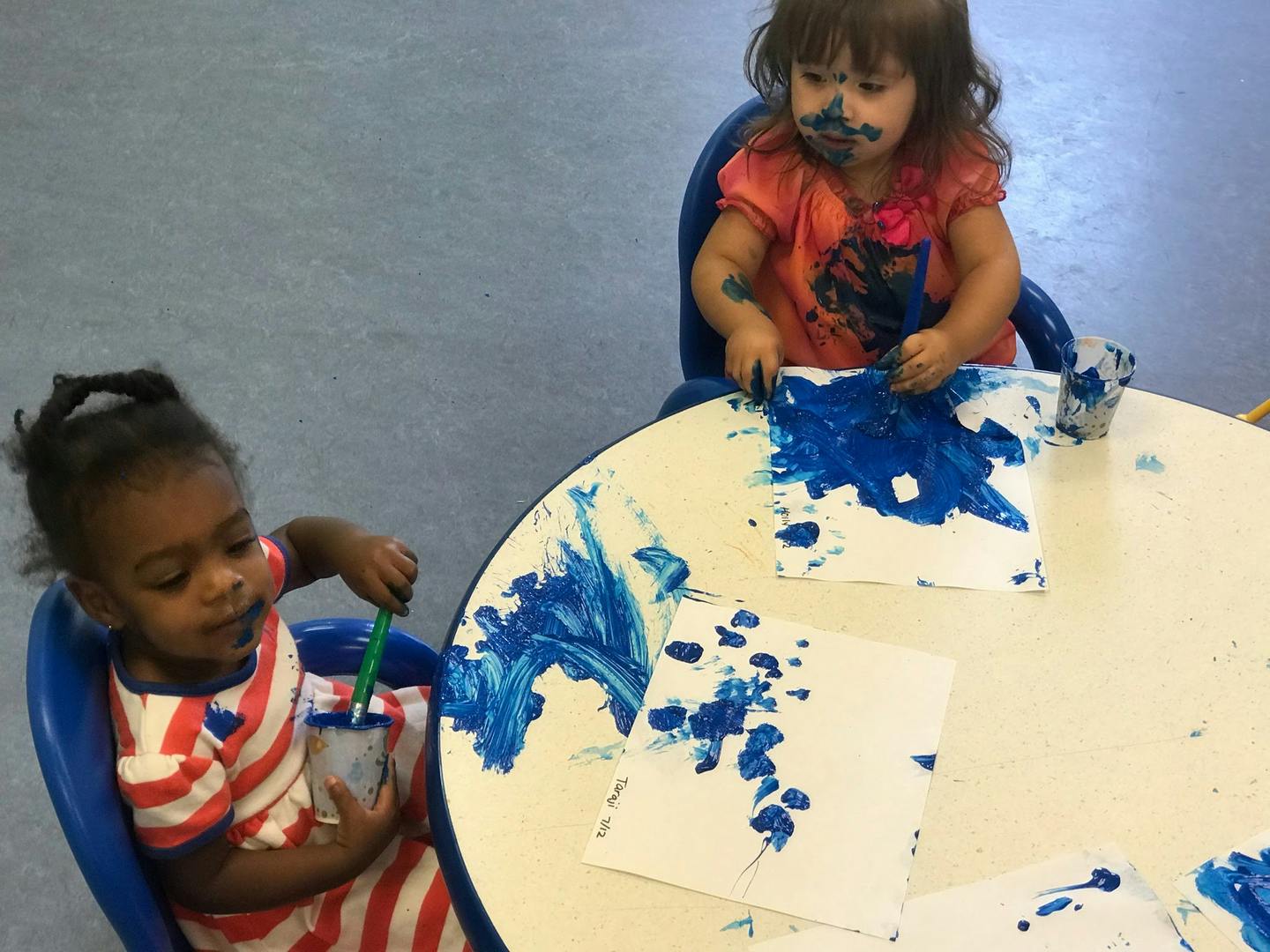 Two children painting with blue paint at a table