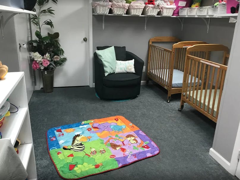 Two cribs, a chair, and a colorful playmat in a room