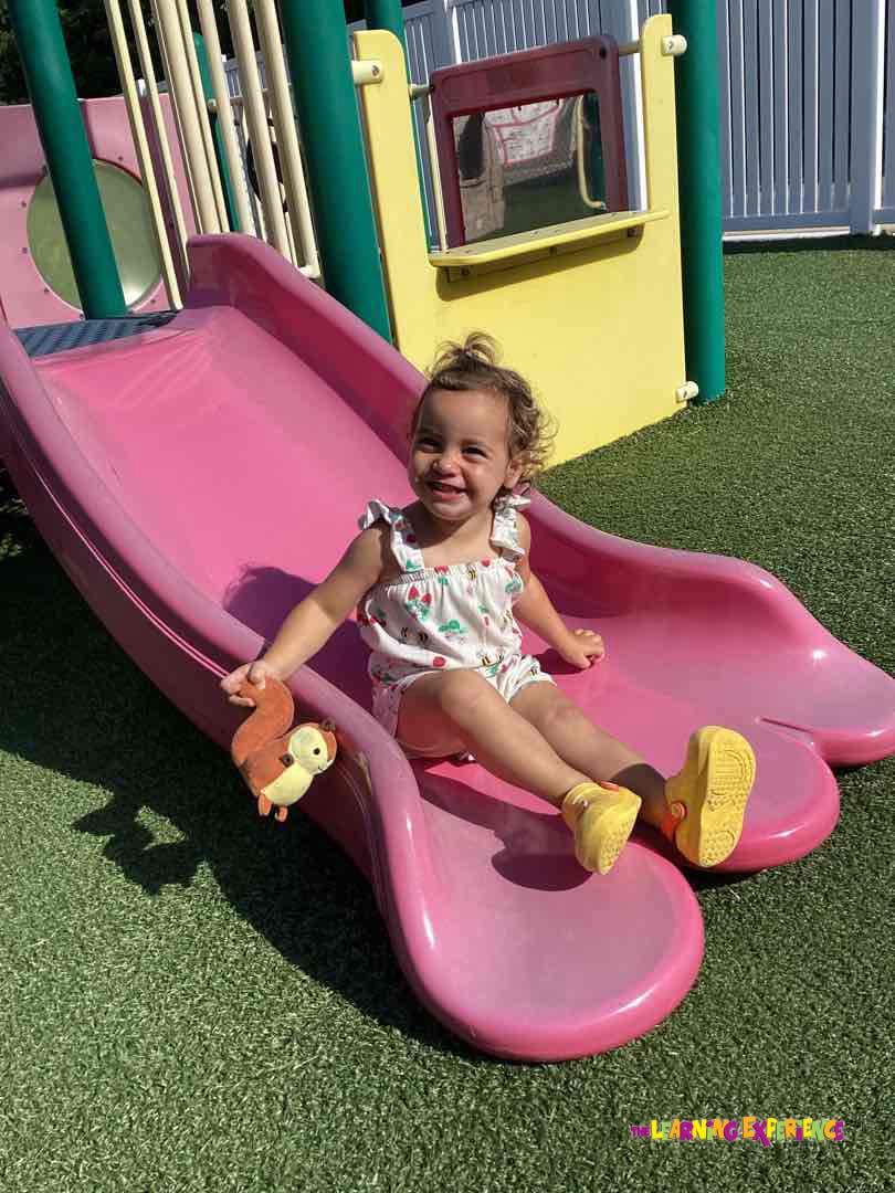 Child sitting on a pink playground slide holding a toy squirrel
