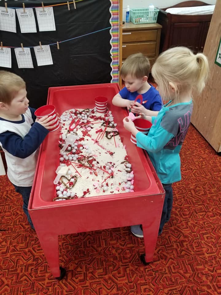 Three children playing at a sensory table in a classroom
