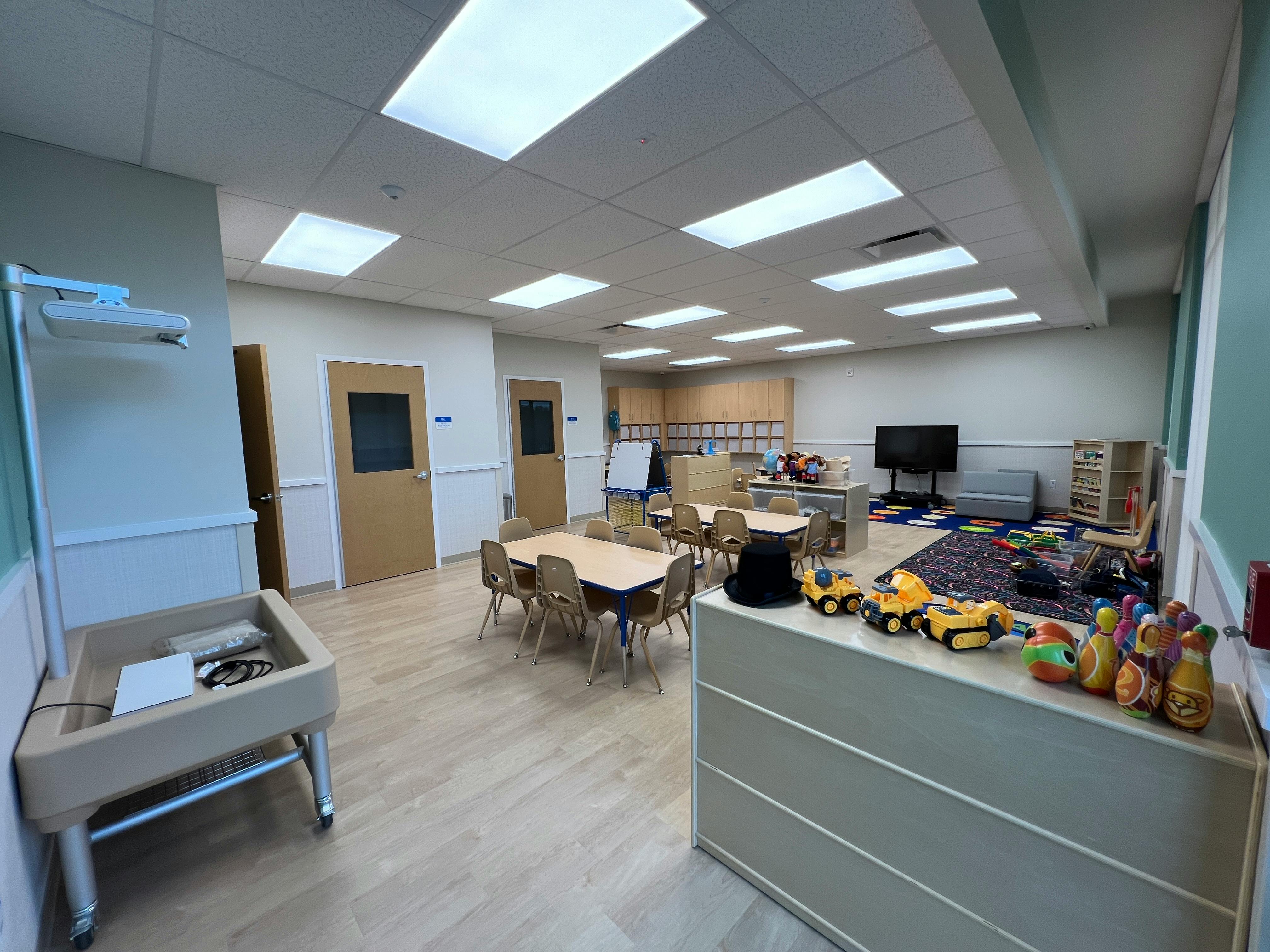 Empty classroom with small tables and chairs, toys on a counter