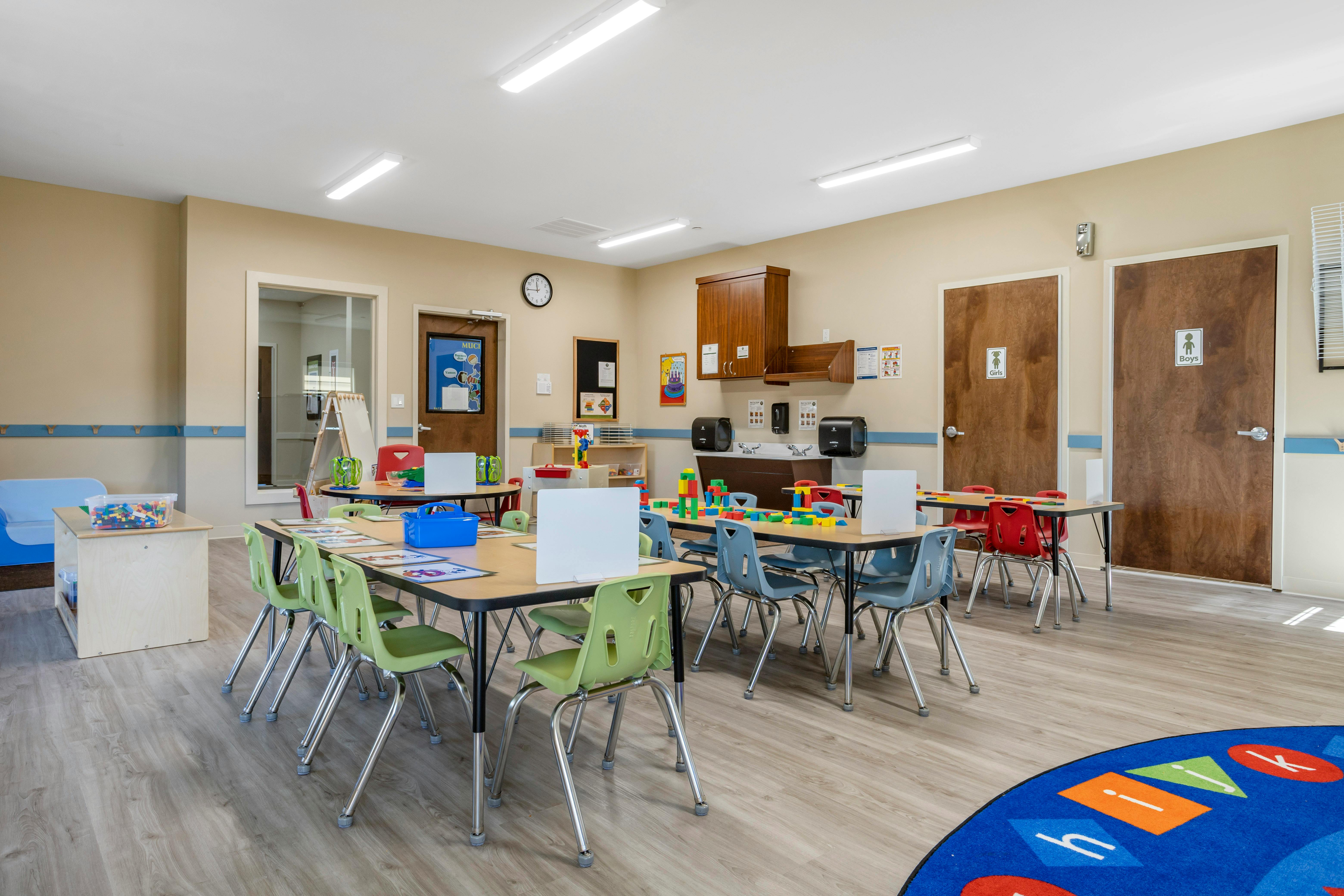 Classroom with child-sized tables and chairs, toys, and two restroom doors