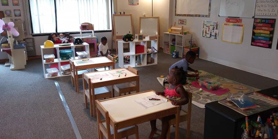 Children in a classroom, one at a desk, two on the floor