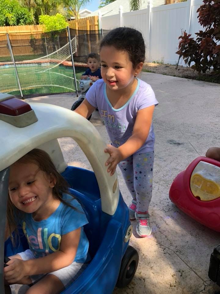 Child sitting in toy car, another child pushing it