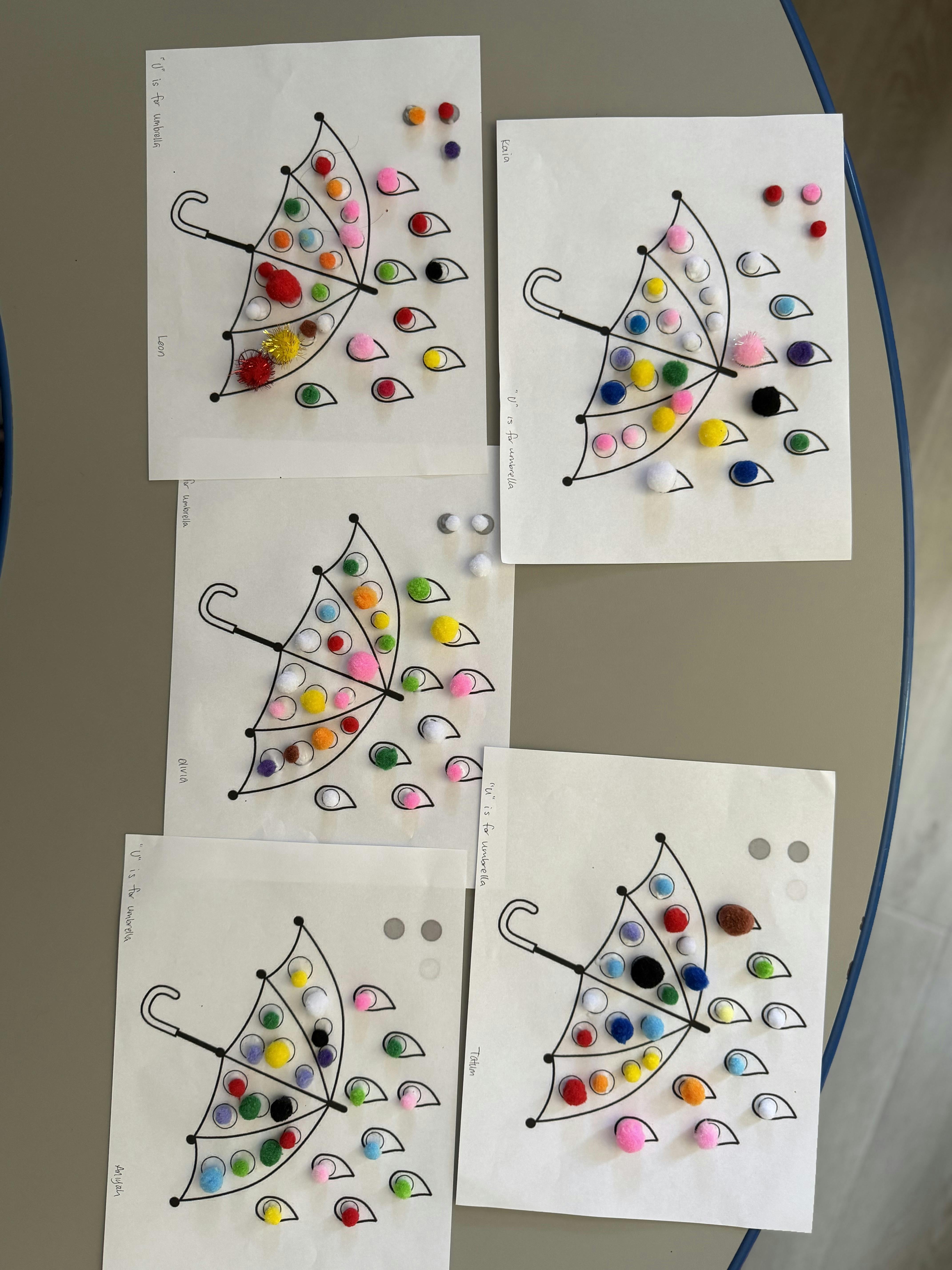 Five umbrella drawings decorated with colorful pom-poms