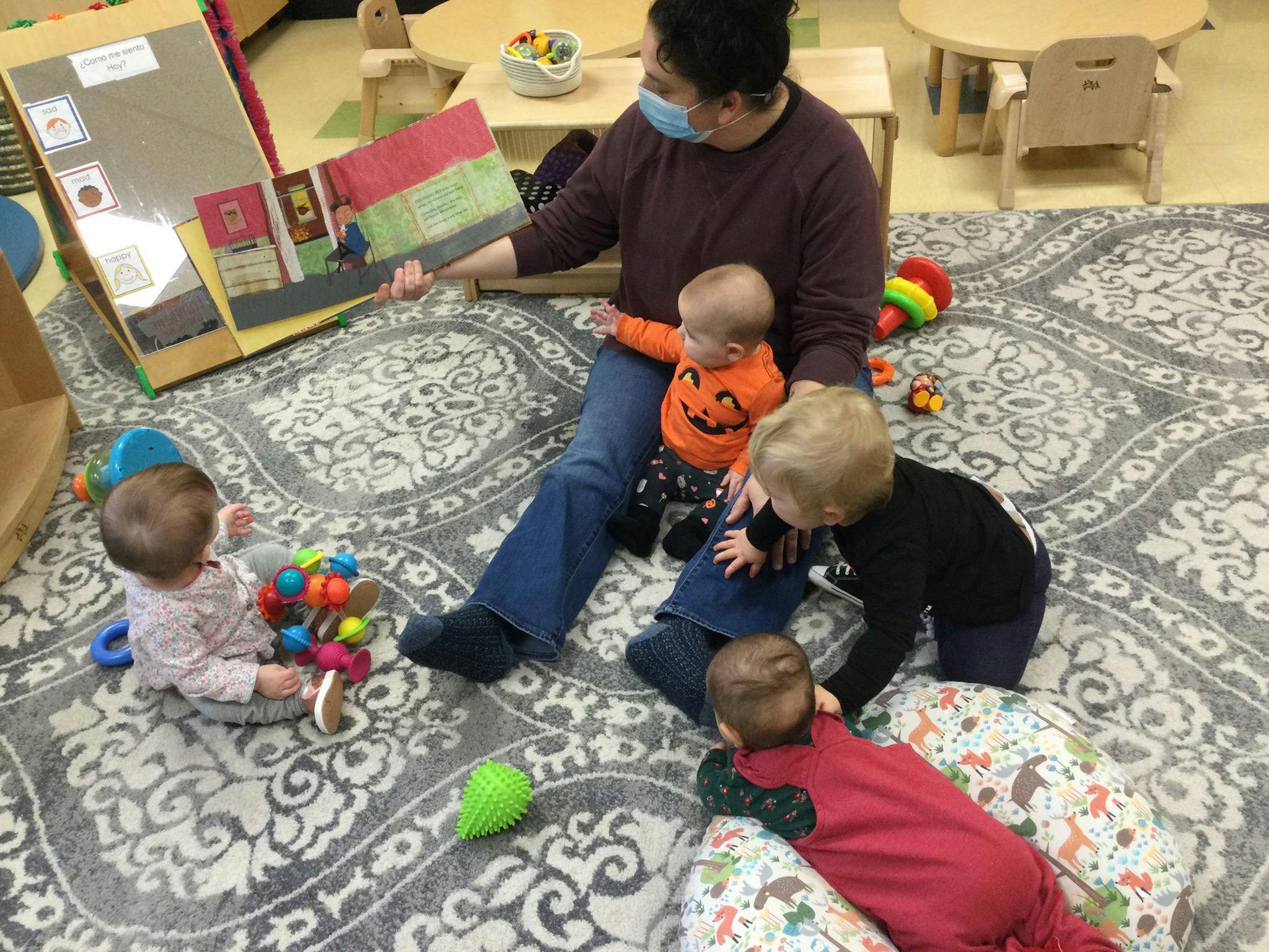 Person reading a book to multiple children on a rug
