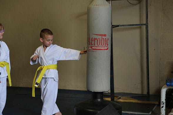 Child in a white uniform with a yellow belt punching a freestanding bag